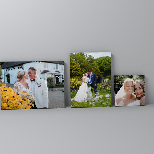 Three wrapped canvas prints of wedding photos leaning against a grey wall